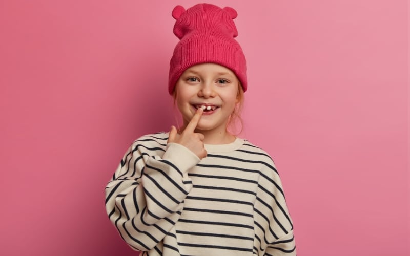 Cheerful funny little girl points at her teeth